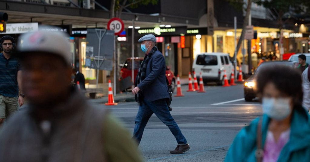Man wearing a mask walks across the street in inner city Auckland