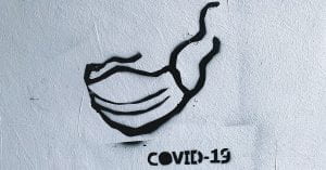 Black graffiti on a white wall with the words "COVID-19" and an image of a face mask