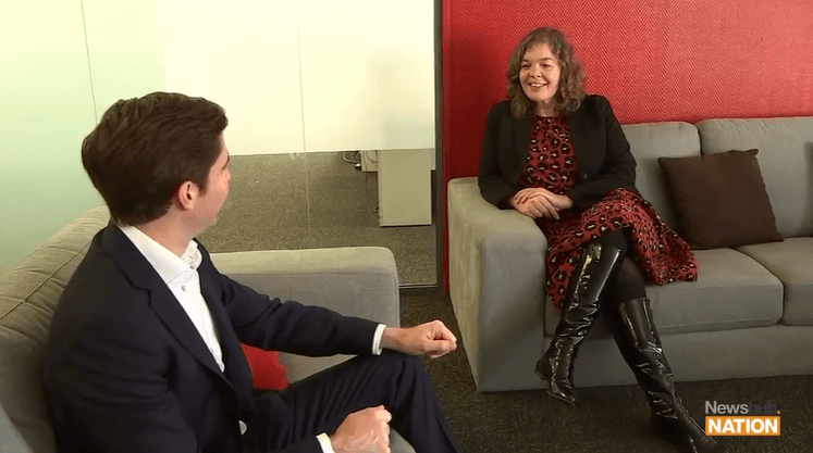 A man sits on a couch interviewing a woman who is smiling