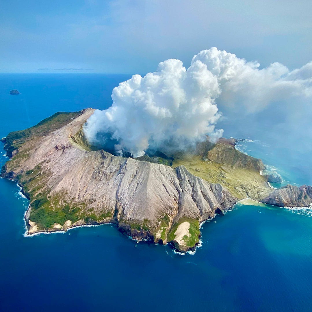 An aerial photo of Whakaari/White Island with an eruption plume emanating from its crater