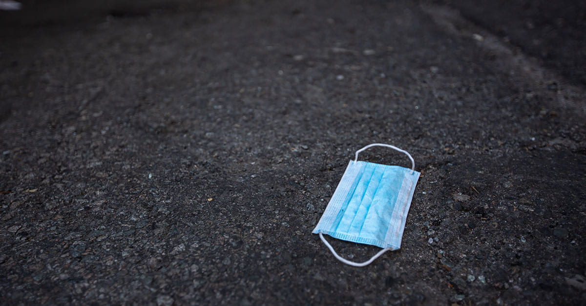 blue surgical face mask discarded on pavement