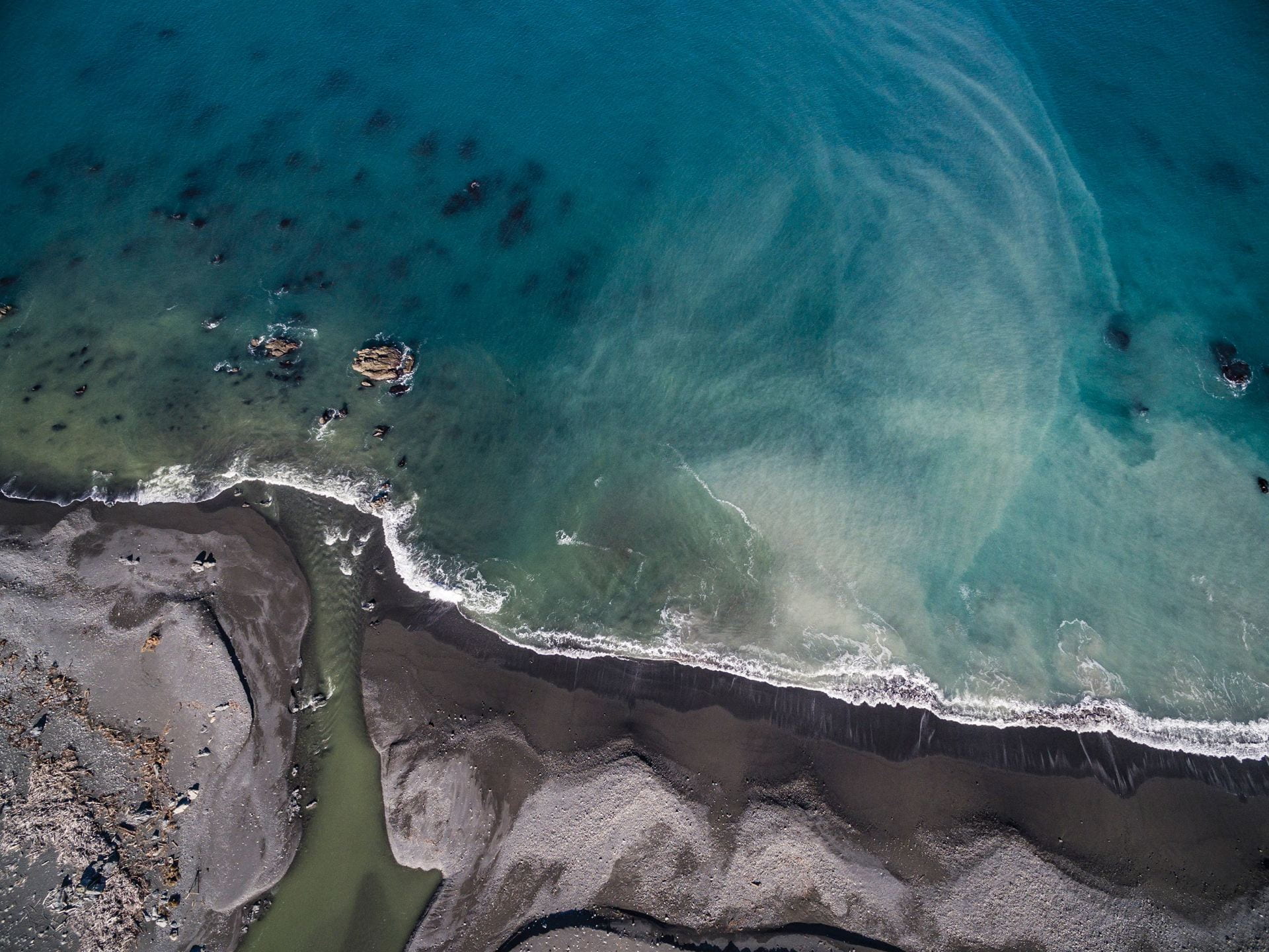 aerial photo of sediment swirling in the sea next to a stony coastline