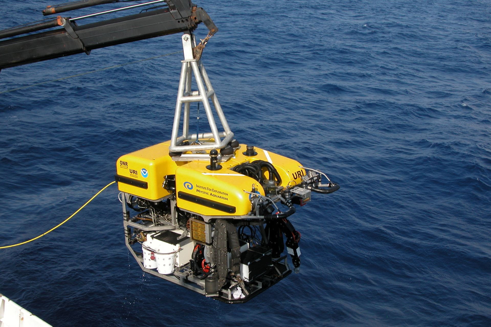 A yellow submersible ROV camera is lowered into the ocean by a winch