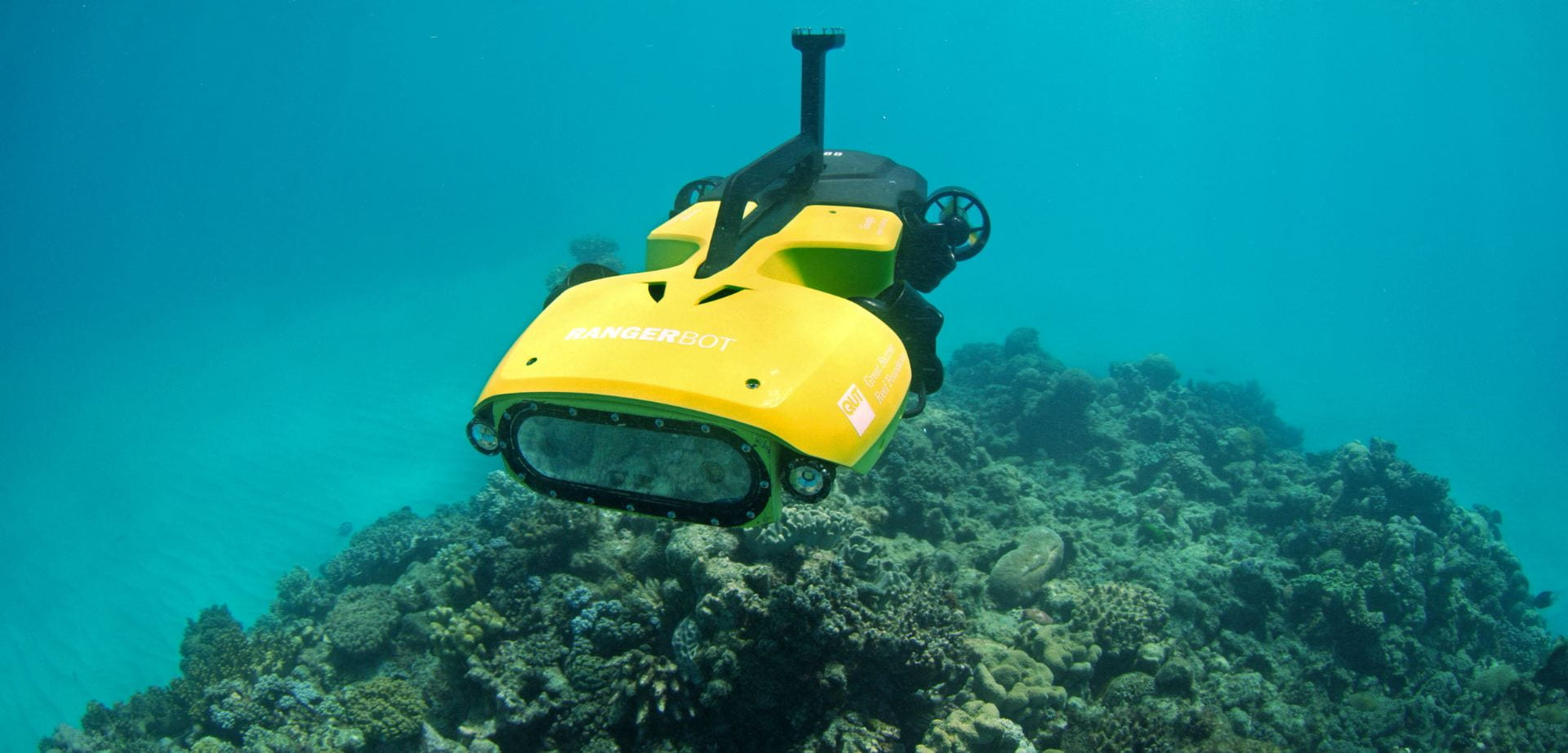 A yellow submersible autonomous vehicle navigates above a coral reef.