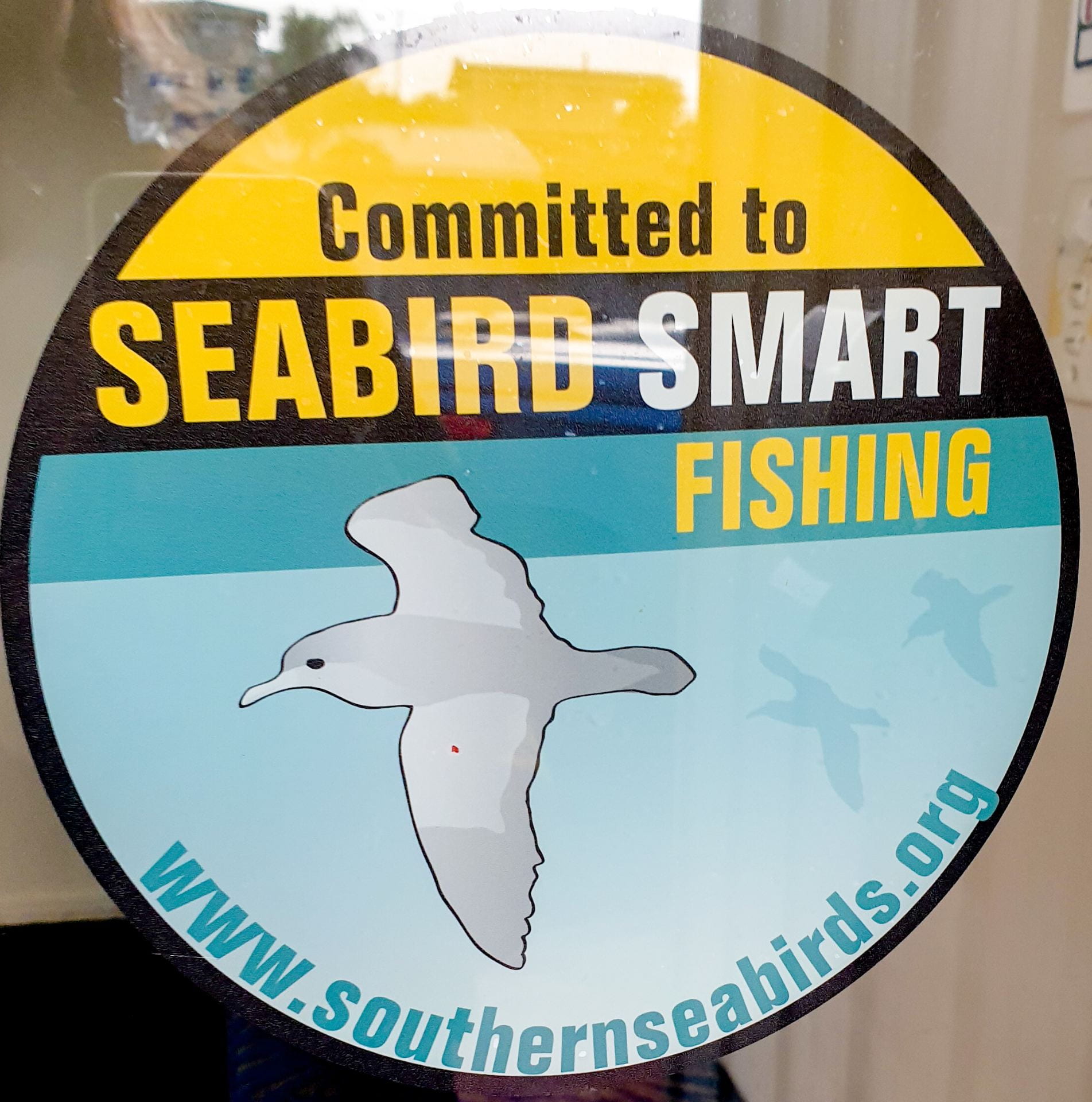 A circular sticker attached to a window with an image of a flying seabird and the words 'Committed to seabird smart fishing www.southernseabirds.org"