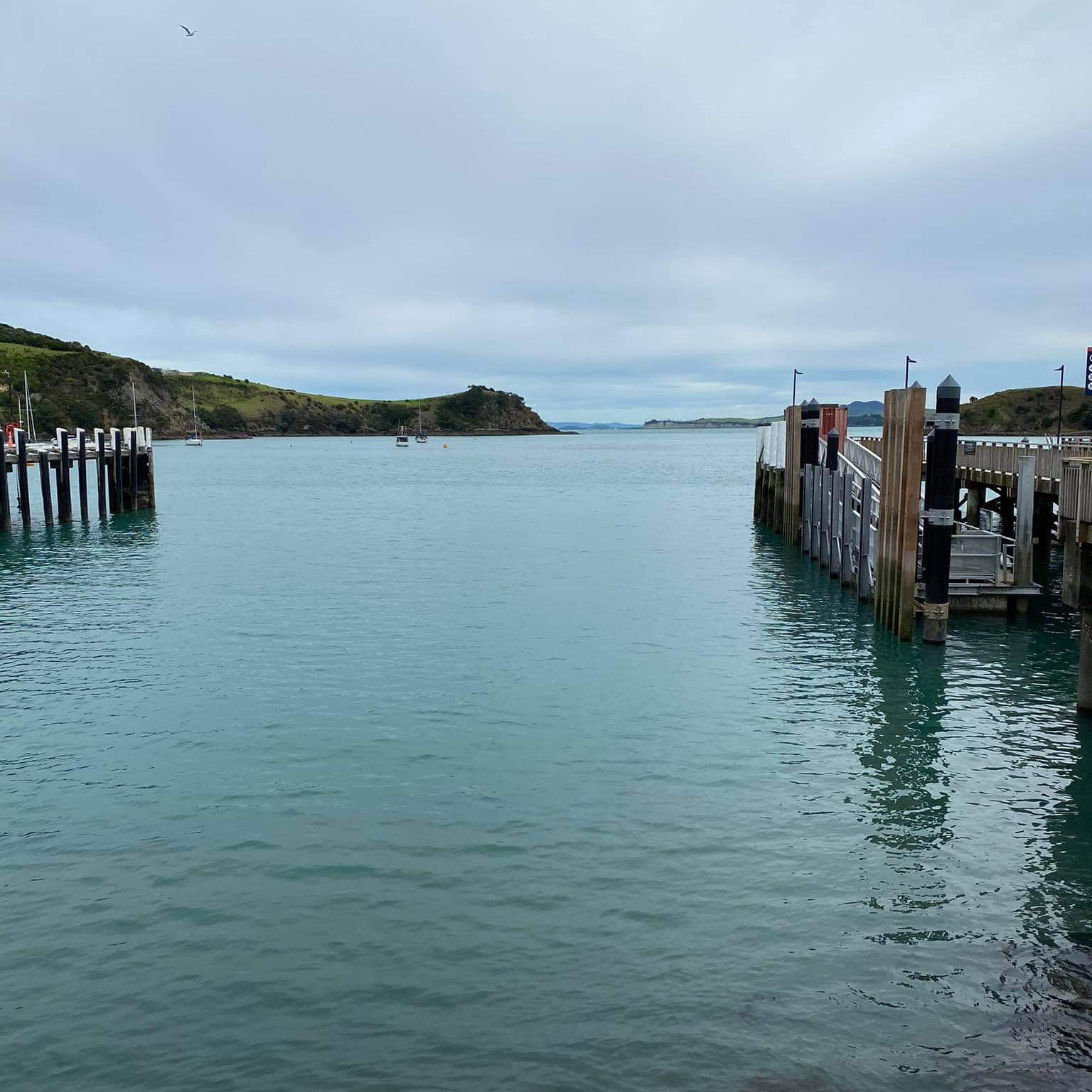 Still harbour water between two jetties beneath a moody grey sky
