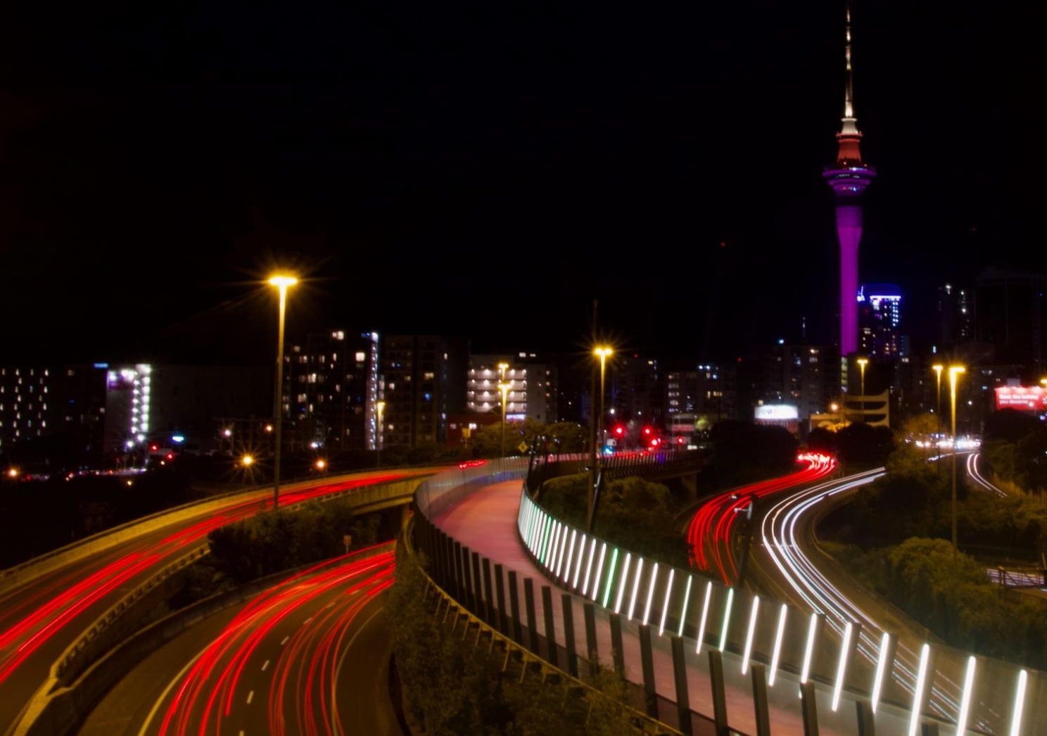 Auckland Sky Tower and cycle path at night. The tower is lit up pink.